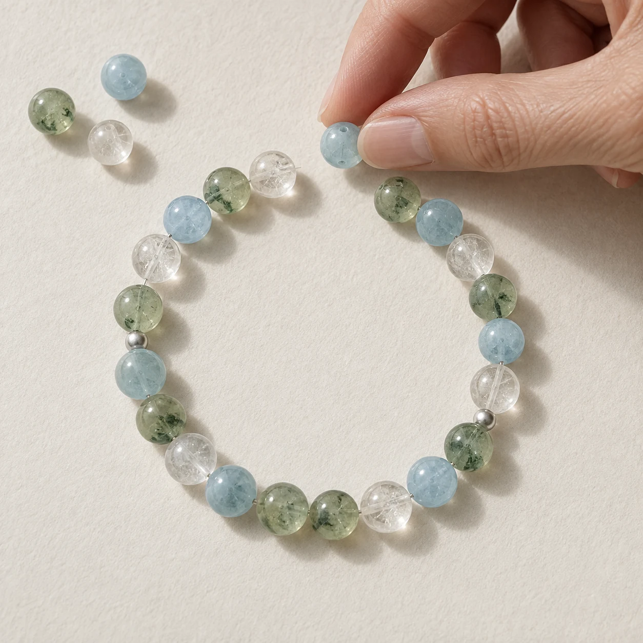 Hand arranging blue, green, and clear crystal beads into a bracelet design