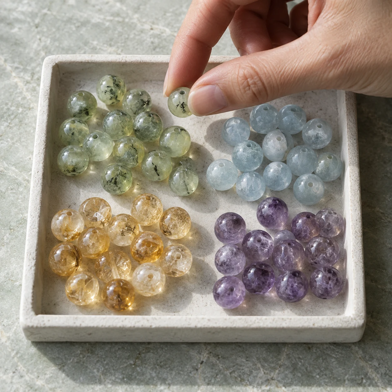 Hand selecting a green crystal bead from blue, gold, green, and purple stones