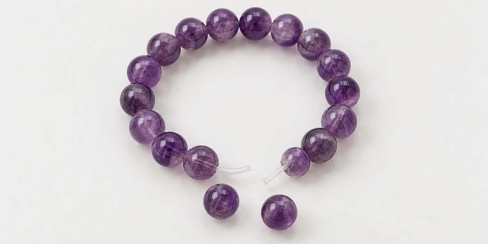 Broken amethyst bracelet with exposed elastic ends and two loose beads on a plain background